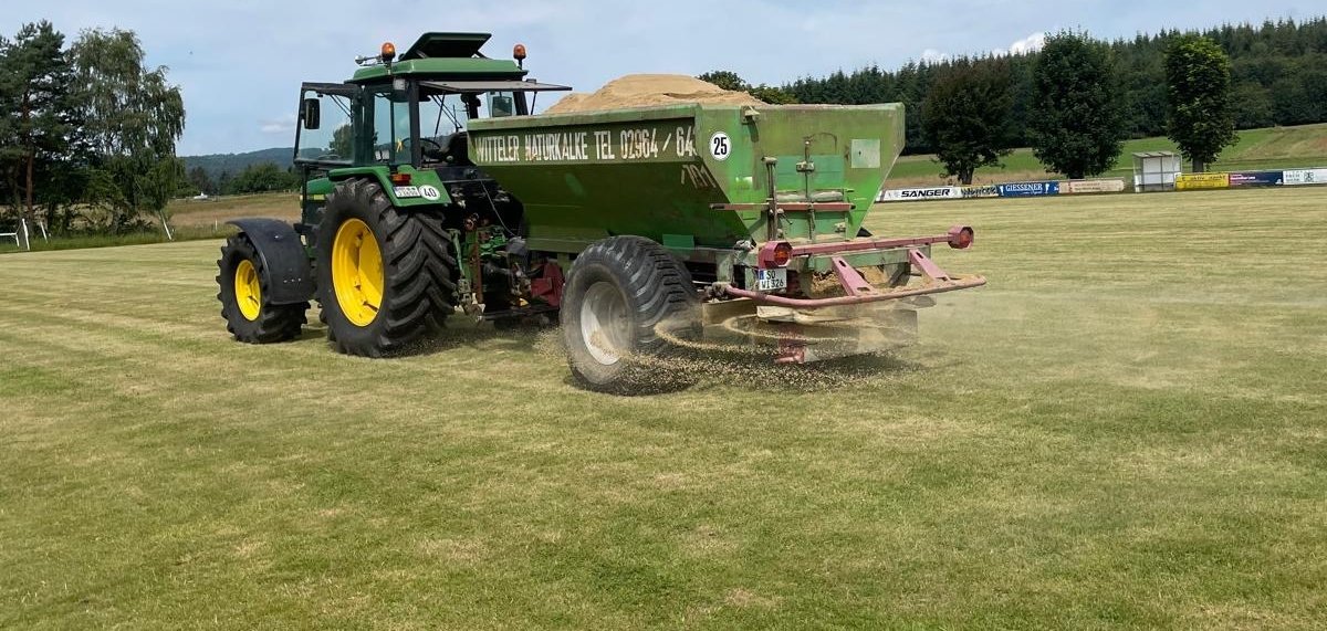 Mit einem Schlepper + Streuer wird der Sand auf der Rasenfläche verstreut