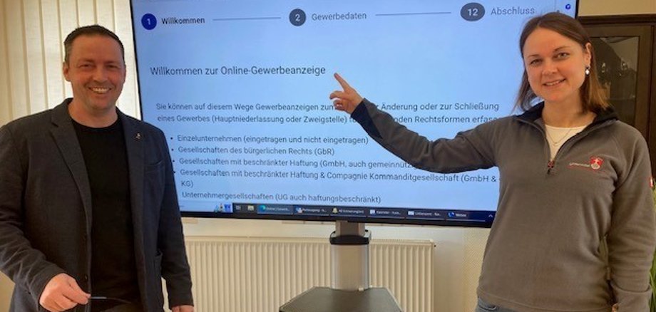Bürgermeister Holger Siemon und Verena Schneider vom Bürgerbüro zeigen den neuen Online-Vorgang am großen Fernsehbildschirm