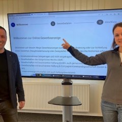 Bürgermeister Holger Siemon und Verena Schneider vom Bürgerbüro zeigen den neuen Online-Vorgang am großen Fernsehbildschirm