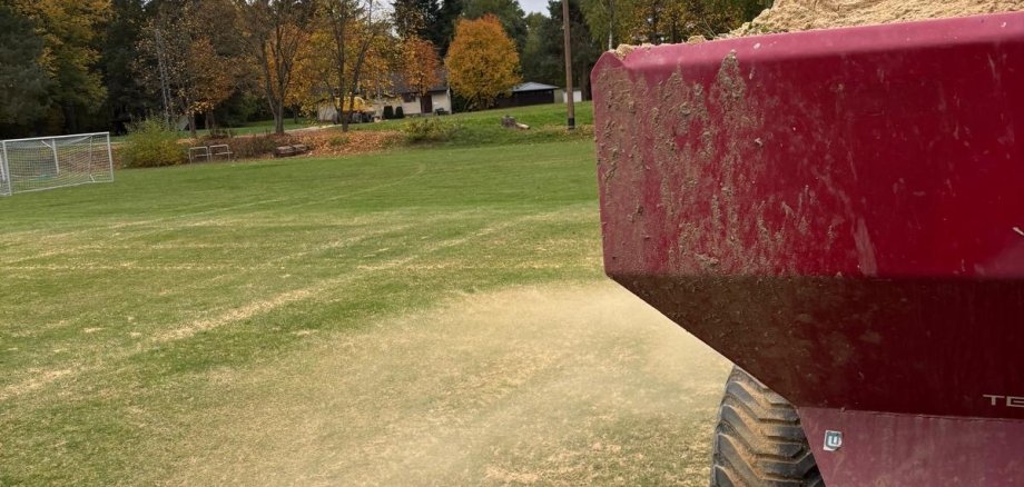 Mit einem Streuer wird der Sand auf dem Sportplatz verteilt